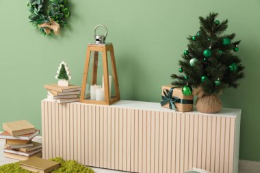 Fenerli Noel ağacı, mumlar, hediye kutusu ve oturma odasındaki yeşil duvarın yanındaki klozette bulunan kitaplar.