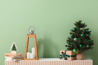 Fenerli Noel ağacı, mumlar, hediye kutusu ve oturma odasındaki yeşil duvarın yanındaki klozette bulunan kitaplar.