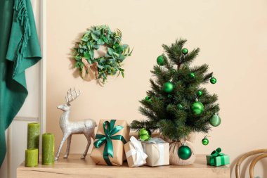 İçinde hediye kutuları, geyikler ve mumlar olan Noel ağacı oturma odasındaki bej duvarın yanında.