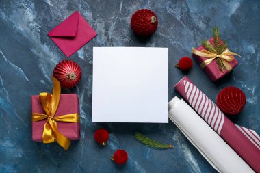 Zarflı boş tebrik kartı, Noel süslemeleri, hediye kutuları ve grunge mavisi arka planda paketleme malzemeleri.