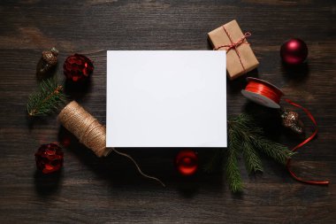 Noel süsleri, ambalaj malzemeleri ve kahverengi ahşap arka planda hediye kutusu olan boş bir tebrik kartı.