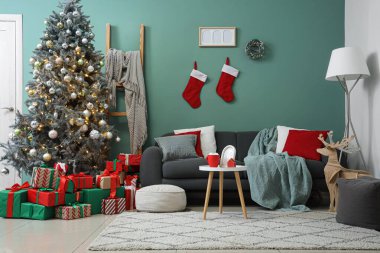 Kanepe, sehpa, lamba, Noel ağacı ve mavi duvarın yanında bir sürü hediye kutusu olan festival odasının içi.