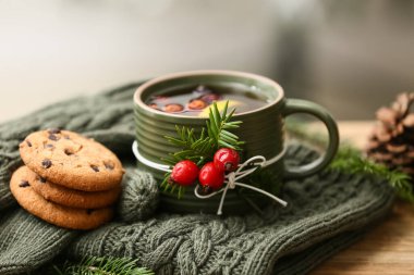 Kış kompozisyonu, ahşap masada lezzetli bir kupa gül, kalça çayı, kurabiye ve kazak, yakın plan.