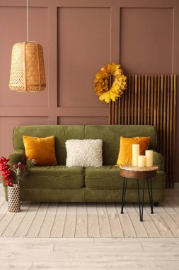 Sonbahar dekorlu bir oturma odası, rahat bir kanepe ve mumlu bir masa.