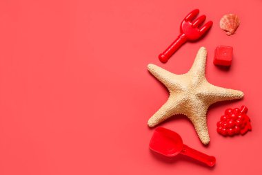 Kumsal kum kalıpları, denizyıldızı, oyuncak tırmık ve kürek kırmızı arka planda.