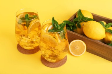 Sarı arka planda nane ve turunçgil meyveli limonlu buzlu çay.