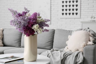 Oturma odasındaki masa üzerinde leylak çiçekleri ve dergiler olan vazo.