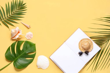 Açık kitaplı kompozisyon, küçük plaj aksesuarları, deniz kabukları ve renk arkaplanda palmiye yaprakları