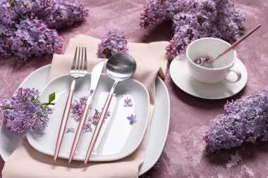 Mor arka planda gümüş çatal bıçak seti ve leylak çiçekleri olan güzel bir masa, yakın plan.