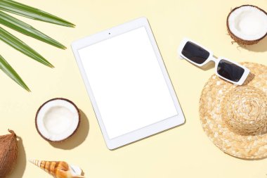 Şapkalı, güneş gözlüklü ve bej arka planda plaj dekoru olan tablet bilgisayar