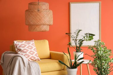 Turuncu duvarın yanında şık bir kanepe ve bitkiler var.