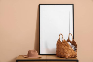 Çantalı şık bir şapka ve bej duvarın yanındaki bankta boş bir çerçeve.