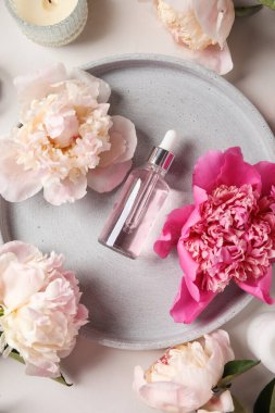 Hafif arka planda güzel şakayık çiçekleri olan bir şişe gerekli yağ.