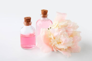 Beyaz arka planda güzel şakayık çiçekleri olan gerekli yağ şişeleri.