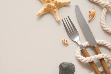 Bej arka planda çatal bıçak, ip ve deniz kabuklarıyla güzel bir masa, yakın plan.