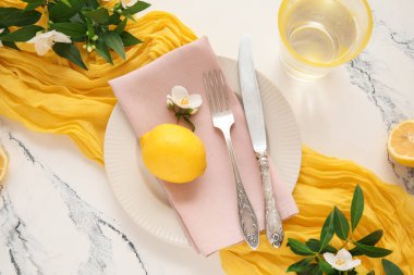 Çatal bıçak, peçete, limon ve yeşil dallarla mermer arka planda güzel bir masa.