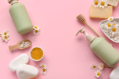 Papatya çiçeğinden yapılmış çerçeve, spa taşları ve pembe arkaplanda kozmetik ürünler, yakın plan