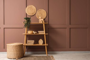 Odadaki kahverengi duvarın yanında bitki ve hasır sepetli kitaplık.