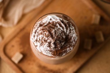 Kahverengi arka planda krem şantili ve pudralı bir bardak kakao.