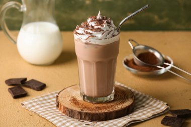 Kahverengi masada yeşil grunge duvarına karşı krem şantili ve çikolata parçalı bir bardak kakao.