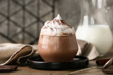 Krem şantili bir bardak kakao, çikolata ve tarçın çubukları kahverengi masada gri grunge duvara karşı.