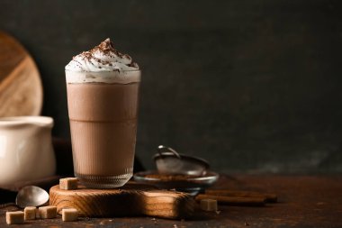 Bir bardak krem şanti ve arkaplanda şeker küpleriyle kakao içeceği.