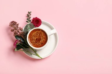 Kasımpatı çiçekli bir fincan kahve ve pembe arka planda okaliptüs dalları.