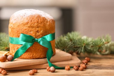 Noel Panettone pastası, fiyonklu, fındıklı ve köknar dallı ahşap masada bulanık arka planda.