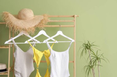 Yeşil duvarın yanında mayo ve yaz şapkası olan raflar.