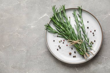 Bir demet taze biberiye, biber ve gri arka planda deniz tuzu tabağı.