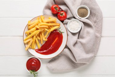 Lezzetli patates kızartması, ketçap, kurutulmuş otlar ve beyaz ahşap arka planda domates tabağı.