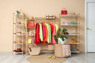 Giysi askısı ve raf üniteleri, soyunma odasındaki bej duvarın yanında aksesuarlar.