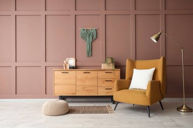 Rahat kahverengi koltuğu, standart lambası ve ahşap dolabı olan şık bir oturma odası.