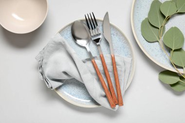 Gümüş çatal bıçak takımı, peçete ve okaliptüs yapraklı tabaklar gri arka planda