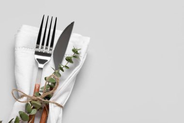 Gri arkaplanda bıçak, peçete ve okaliptüs dallı gümüş çatal.