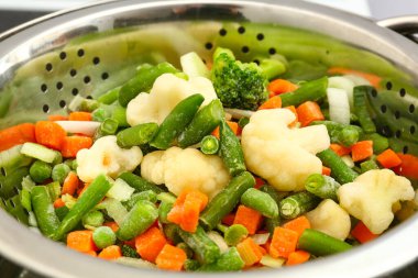 Metal kevgire buharlaşan donmuş sebzeler, yakın plan.