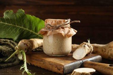 Yabanturpu soslu kavanoz, ahşap arka planda kök ve yaprak.