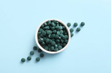 Mavi arka planda bir kase spirulina tableti.