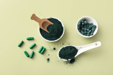 Yeşil arka planda ahşap kepçeyle kaplanmış spirulina tozu ve tabletler.