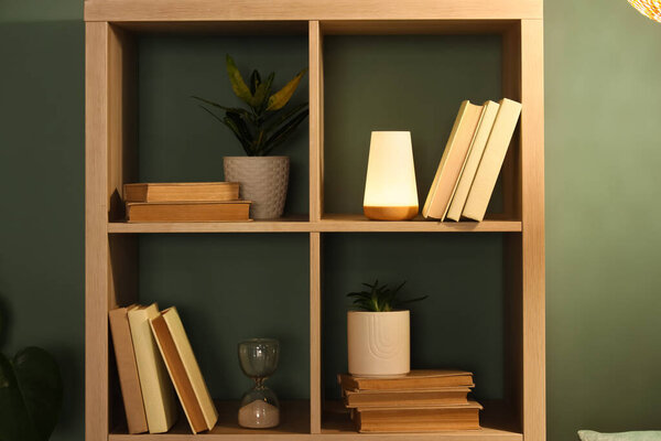 Bookshelf with plant and glowing lamp near green wall in room
