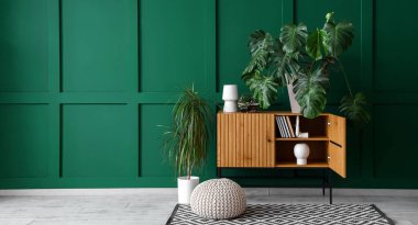 Odanın içinde ahşap klozet ve yeşil duvarın yanında bitkiler var. Tasarım için pankart