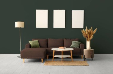 Rahat bir kanepe, masa ve lamba odada koyu yeşil duvarın yanında.