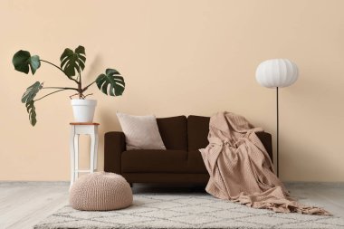 Oturma odasının içinde kahverengi kanepe, lamba, puf ve bitki var.