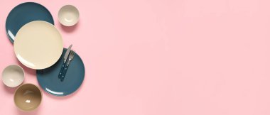 Pembe arkaplanda farklı tabak ve çatal bıçak takımları.