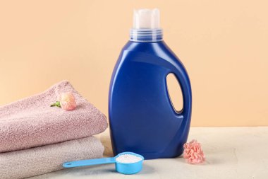 Çamaşır deterjanları, karanfil çiçekleri ve katlanmış havlular bej arka planda.