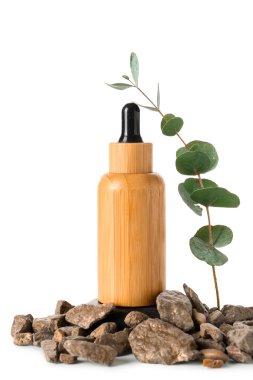 Kozmetik yağlı ahşap şişe, okaliptüs dalı ve beyaz zemin üzerinde taşlar