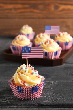 Kahverengi ahşap duvarın yanındaki siyah masada ABD bayraklı lezzetli vatansever çörekler. Amerikan Bağımsızlık Günü