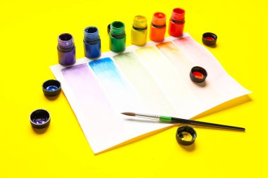 Sarı arkaplanda farklı boya, fırça ve gökkuşağı renk paletine sahip kompozisyon