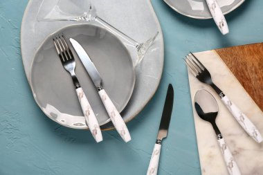 Temiz tabaklar, kesim tahtası, cam ve çatal bıçak takımı mavi grunge masasında.