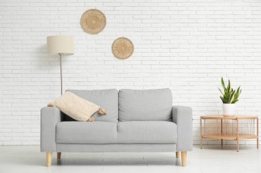 Beyaz tuğla duvarın yanında kanepesi, masası ve bitkisi olan oturma odasının içinde.